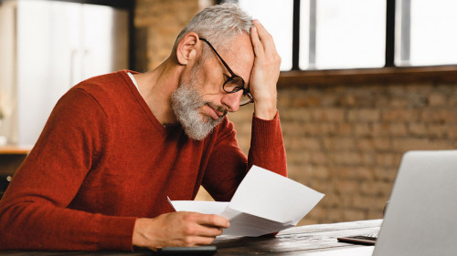 Expensive charges on domestic bills. Loan, debt, bunkruptcy concept. Sad depressed caucasian businessman holding documents, having problems with dismissal at home office