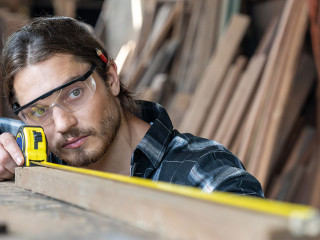 Male carpenter using measuring tape at the carpentry workshop. J