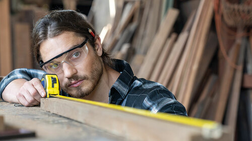 Male carpenter using measuring tape at the carpentry workshop. J