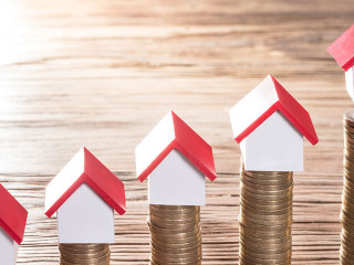 Person Placing House Models On Stacked Coins