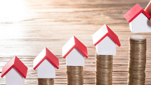 Person Placing House Models On Stacked Coins