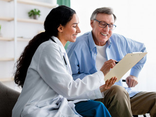 Young doctor asking senior impaired male patient in wheelchair to sign insurance policy at home