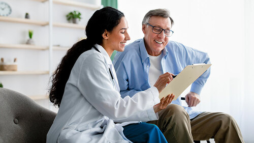 Young doctor asking senior impaired male patient in wheelchair to sign insurance policy at home
