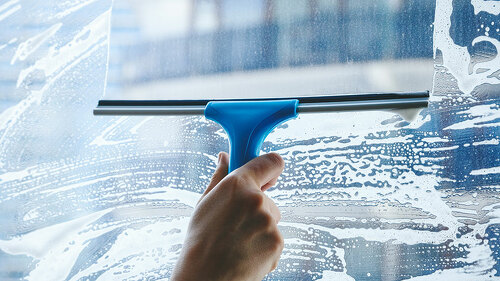 young female hand cleaning dirty glass window with a squeegee