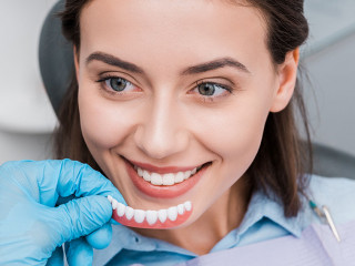 cropped view of dentist holding prosthesis near happy girl in dental clinic