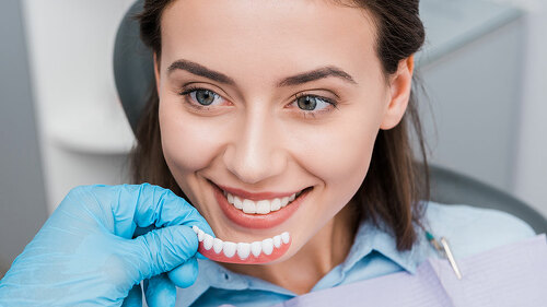 cropped view of dentist holding prosthesis near happy girl in dental clinic