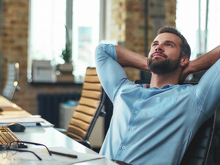 Enjoying break. Satisfied young bearded businessman leaning back with hands behind head and relaxing while sitting in the modern office