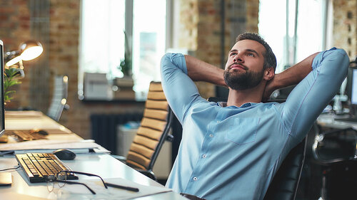 Enjoying break. Satisfied young bearded businessman leaning back with hands behind head and relaxing while sitting in the modern office