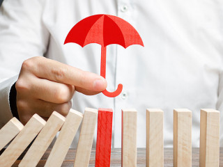 A businessman insures red dominoes and stops the collapse of the whole system. Insurance and risk management. Accurate forecasts and miscalculations. Financial support, subsidies and exemptions