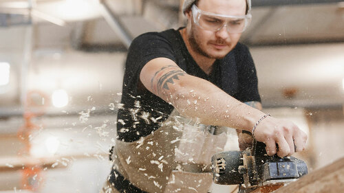 Carpenter working with electric planer on wooden plank in workshop. Hands and planer close up.