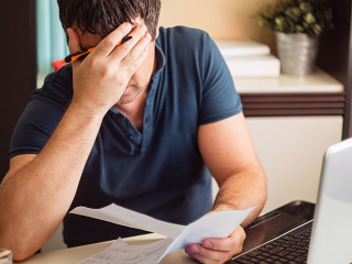 The shocked and disappointed man saw the bad news in the invoices. Frustrated unemployed man with documents.