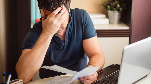 The shocked and disappointed man saw the bad news in the invoices. Frustrated unemployed man with documents.