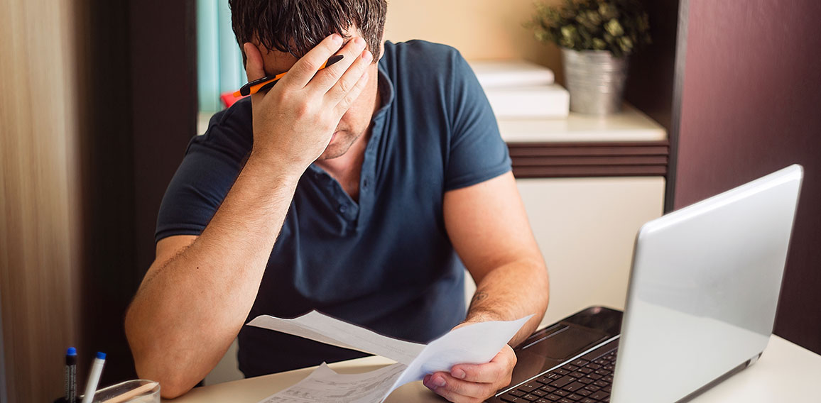 The shocked and disappointed man saw the bad news in the invoices. Frustrated unemployed man with documents.