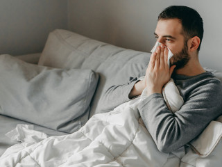 Young sick bearded european man sneezes into napkin at home on g