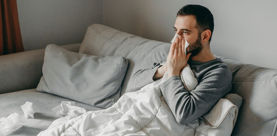 Young sick bearded european man sneezes into napkin at home on g