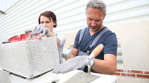 Mason with trainee in construction, building wall