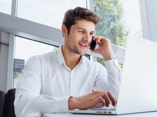 Happy young businessman talking on cell phone and using laptop