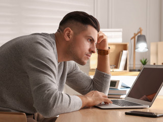 Man with poor posture using laptop at table indoors