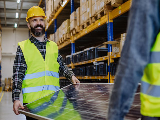 Warehouse workers in reflective vests carring a solar panel.