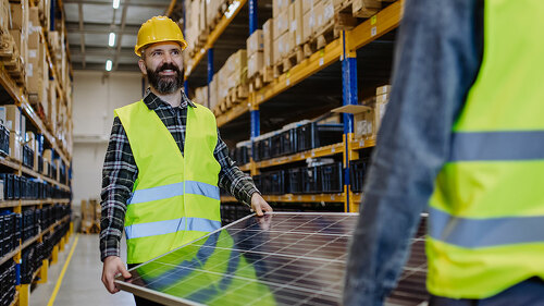 Warehouse workers in reflective vests carring a solar panel.