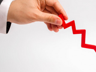 A businessman's hand is holding a red arrow down on a white background. The concept of reducing costs and profits, falling living standards and prices. Decreased projections, depressed economies.