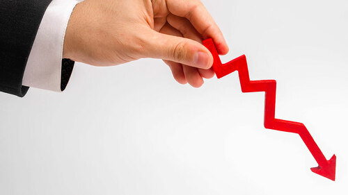 A businessman's hand is holding a red arrow down on a white background. The concept of reducing costs and profits, falling living standards and prices. Decreased projections, depressed economies.