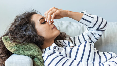 Upset depressed young woman lying on couch feeling strong headac
