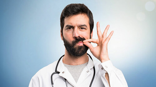 Young doctor making silence gesture on blue background