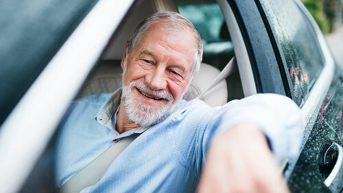 Happy senior man sitting in car in driver seat.