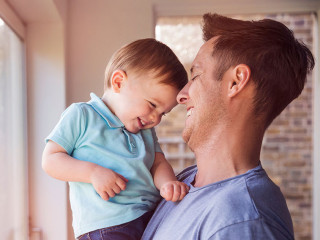 Father holds toddler son while drinking coffee at home, by the w