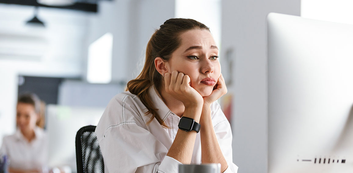 Bored young woman dressed in shirt sitting at her workplace