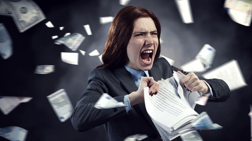 Young stressed woman ripping documents with frustrated facial expression.