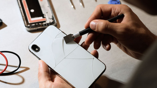 Technician repairing broken smartphone at table, closeup