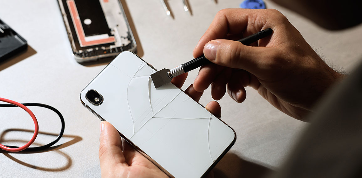 Technician repairing broken smartphone at table, closeup