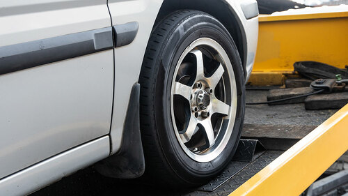 Broken down car towed onto flatbed tow truck with hook cable