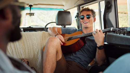 Man with guitar, music in van and smile on travel vacation road trip together with friends. Group holiday in summer, relax and happy musician singing with instrument on a countryside safari adventure