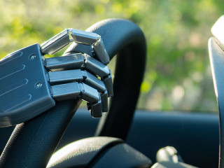 Robot arm on a steering wheel. Artificial intelligence drives a car. Autonomous vehicle concept.
