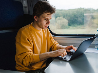 Young male freelancer in orange sweatshirt working on laptop in