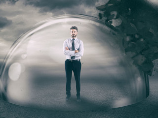 Businessman safely inside a shield dome during a storm that protects him from a wrecking ball. Protection and safety concept