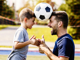 man with child playing football outside on field
