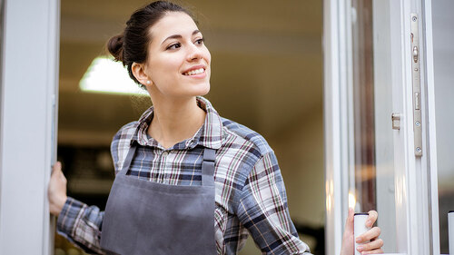Beautiful asian woman store owner with standing in the doorway of her coffee shop looking at camera and smiling.Portrait of girl waitress wearing apron and standing in front
