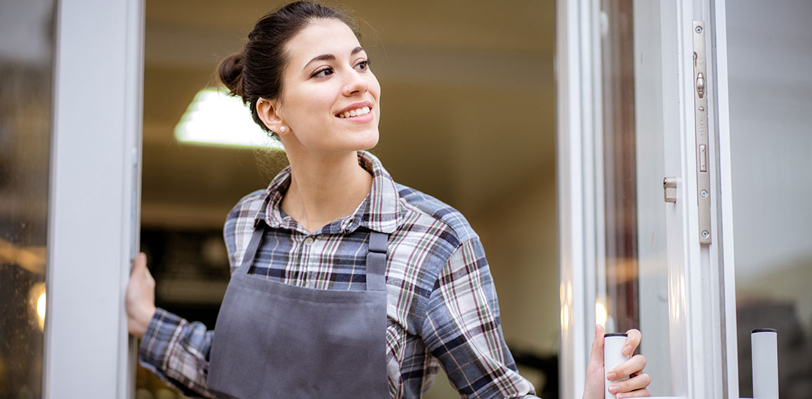 Beautiful asian woman store owner with standing in the doorway of her coffee shop looking at camera and smiling.Portrait of girl waitress wearing apron and standing in front