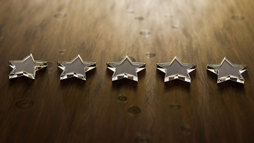 Five star rating - five transparent acrylic glas stars lying on a wooden table. Selective focus and copy space.