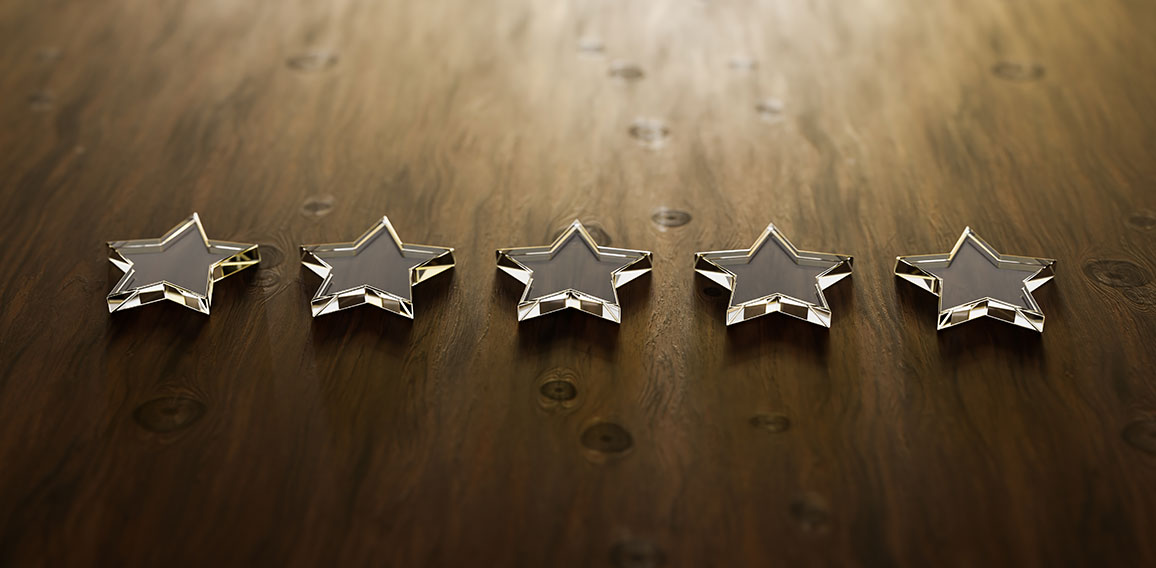 Five star rating - five transparent acrylic glas stars lying on a wooden table. Selective focus and copy space.