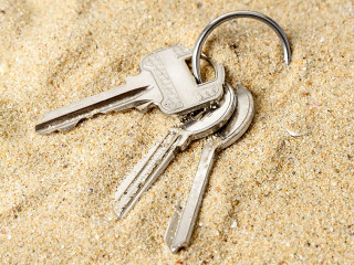 Ring with three home keys on a sea sand. Forget or fall house keys while relaxing on the beach. Accidentally drop keys. Lose bunch of apartment keys concept.