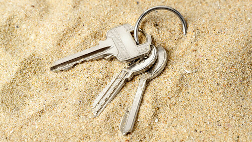 Ring with three home keys on a sea sand. Forget or fall house keys while relaxing on the beach. Accidentally drop keys. Lose bunch of apartment keys concept.
