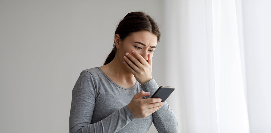 Upset depressed millennial pretty woman covering her mouth with hand and looking at phone