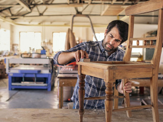 Furniture maker sanding a chair on workshop bench