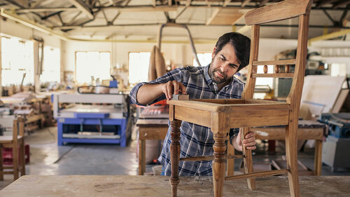 Furniture maker sanding a chair on workshop bench