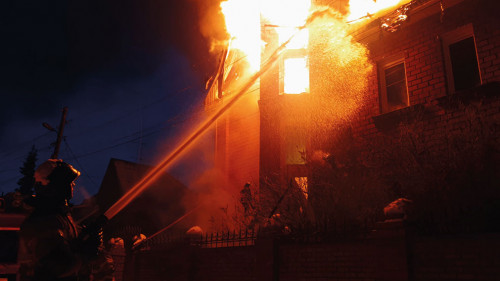 The roof of the house is on fire. The residential building burn, village. Firefighters put out a fire from the crane from above. Smoke and sparks.